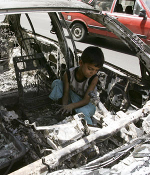 Boy plays inside a burnt car on Haifa street, one day after U.S. soldiers and Iraqi troops clashed with gunmen in Baghdad, 24 June 2004 (REUTERS)