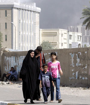 Black smoke rises in the distance from Haifa Street as Iraqis walk home after heavy clashes in central Baghdad on Friday, 23 June 2006 (EPA)