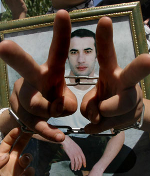Handcuffed, a Palestinian demonstrator holds a photograph of a relative being held in an Israeli jail during a protest outside the offices of the International Committee of the Red Cross, Hebron, 27 June 2006 (AFP)
