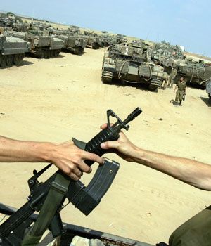 An Israeli soldier passes an M-16 rifle to another one as they stand on a truck next to a line of armored vehicles in a field at a gathering point near Kibbutz Mefalsim, southern Israel, just outside the Gaza Strip, June 29, 2006 (AP)