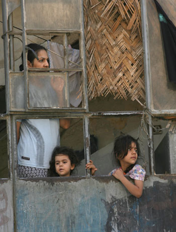 An Iraqi family watch from a window as local people gathers around the wreckage in the street following an early morning car bomb (AFP)