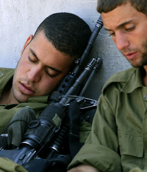 Israeli soldiers rest in the shade of the wall separating the northern Gaza Strip from Israel near the Israeli village of Netiv Ha'asara, July 3, 2006 (AP)