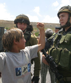 A Palestinian boy shows off his muscles to Israeli soldiers as foreigners and Palestinians demonstrate against the construction of the controversial separation barriers in al-Khader village close to Bethlehem, 07 July 2006 (AFP)