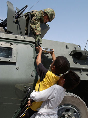 A member of the Japanese coalition forces takes drink of water from a young Iraqi (AP)