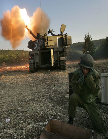 Israeli soldiers cover their ears as a mobile artillery piece fires into Lebanon(AFP)