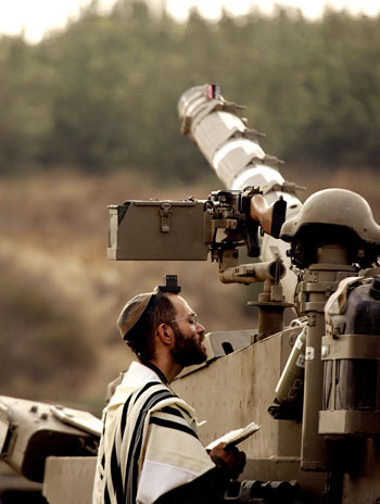 Israeli soldier prays by his tank along the Israeli-Lebanese border (AFP)
