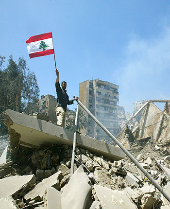 A Hezbollah member waves a Lebanon's national flag as he stands on a destroyed building in a southern suburb in Beirut (R)