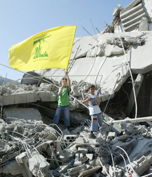 Shiite Muslim Lebanese boys hold up a Hezbollah flag above the rubble of a destroyed house in the Iqlim al-Touffah region of southern Lebanon, in the mountains above the province of Nabatiyeh, 15 August 2006 (AFP)