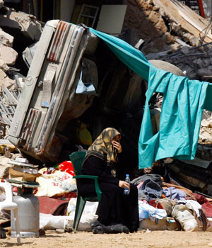 A Lebanese woman sits next to her home, which was damaged during the recent conflict between Israel and Lebanon's Hezbollah, in a southern suburb of Beirut, August 24, 2006 (REUTERS)