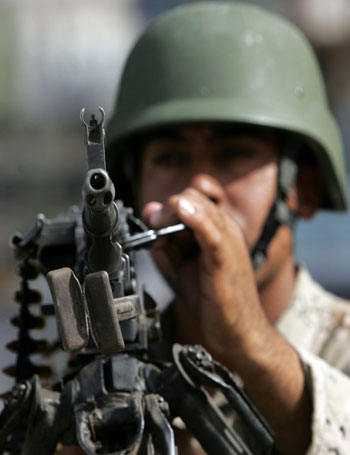 A soldier holds a weapon while manning a checkpoint in Baghdad (R)