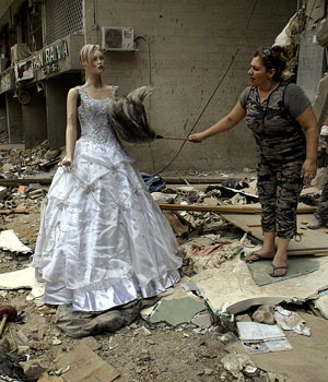 A Lebanese woman removes dust from a wedding dress outside her partially destroyed shop in devastated Beirut's southern suburb, 28 August 2006 (AFP)