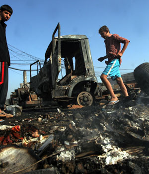 Iraqis walk past a burnt vehicle, after a roadside bomb attack, in Baghdad, Iraq, Sept. 9, 2006 (AP)
