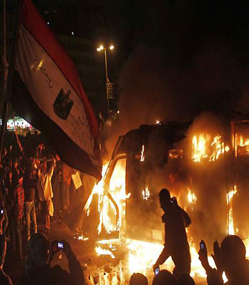 Egyptian protesters stand near a burning vehicle of the security forces as protests and clashes continue in central Cairo, Egypt, 28 January 2013. (EPA)