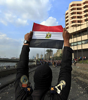 A police officer holds the Egyptian national flag during clashes with anti-government protesters, background, near Tahrir Square. (AP)