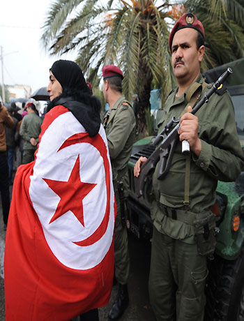 A woman wrapped in a national flag walks past a Tunisian soldier standing guard during late opposition leader Chokri Belaid's funeral procession on February 8, 2013. (AFP)