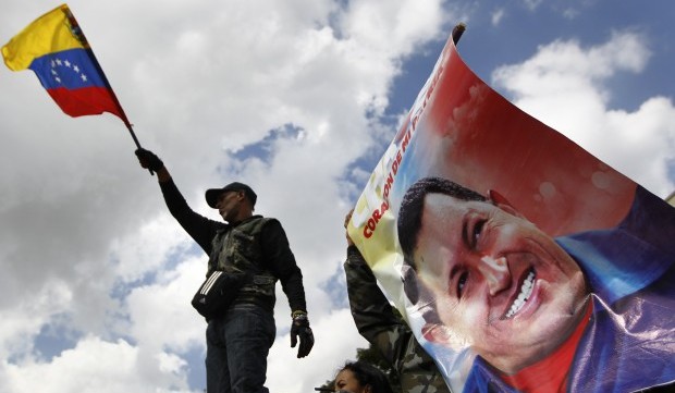 A supporter of Venezuela's President Hugo Chavez waves a national flag next to a giant picture of Chavez, in front of a military hospital where Chavez is being treated, in Caracas February 19, 2013. (Reuters)