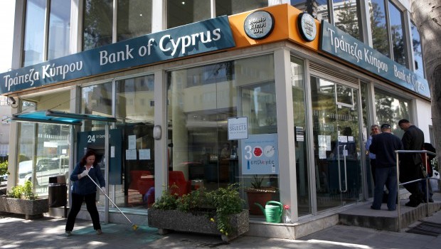 A woman sweeps as people, right, wait outside a branch of Bank of Cyprus in Nicosia, Cyprus, Thursday, March 28, 2013. (AP Photo/Petros Karadjias)