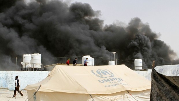 Syrian refugees watch as a fire sends black smoke rising over the Zaatari  refugee camp in northeast Jordan, Friday, March 8, 2013. (AP Photo: Raad Adayleh)