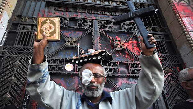 An Egyptian supporter of the April 6 movement with a toytank on his head holds a cross and Islam's Holy book Koran outside the Superior Court building during a demonstration to mark the anniversary of the Muslim brotherhood movement's establishment in Cairo on April 6, 2013.(AFP)