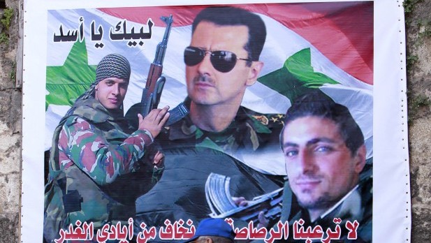 This Tuesday, April 30, 2013 photo shows a large poster of Syrian President Bashar Al-Assad, center, and two Alawite fighters killed in Syria. The Arabic writing that reads, "At your service, oh Assad," and, "Bullets will not terrify us and we are not scared of traitors." (AP Photo/Bilal Hussein)