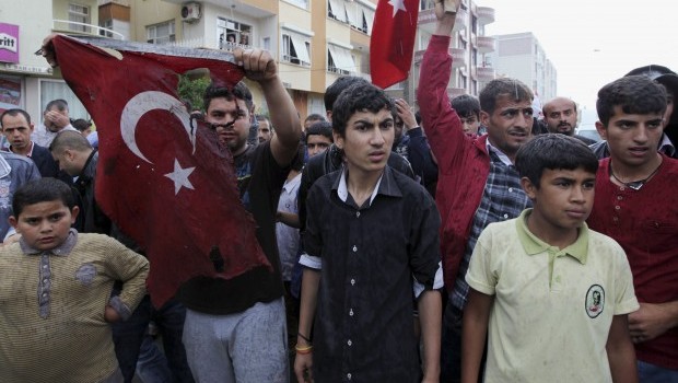 Turkish people display a damaged national flag found in the debris of a destroyed shop as they stage an anti-government protest near the scene at one of the Saturday explosion sites that killed 46 and injured about 50 others, in Reyhanli, near Turkey's border with Syria, on Monday, May 13, 2013. (AP Photo/Burhan Ozbilici)