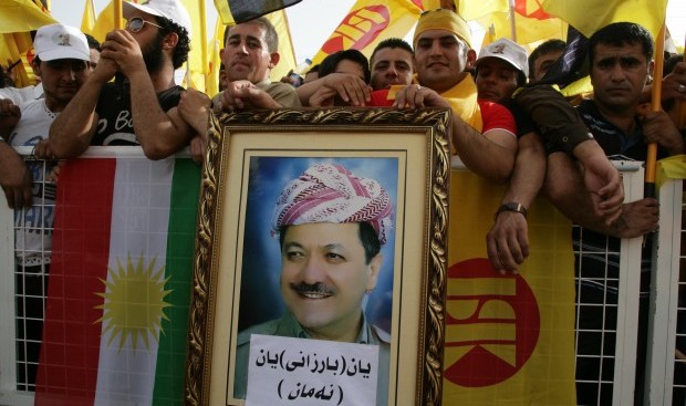 Massoud Barzani (portrait), the president of the Kurdish regional government in northern Iraq and leader of the Kurdistan Democratic Party, wave the party's flag (R) and the Kurdish flag (L) as he delivers a speech in the northern Iraqi Kurdish city of Arbil on May 26, 2013.  AFP/Safin Hamed)