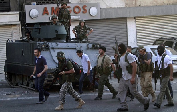 Gunmen and followers of hardline Sunni cleric Sheik Ahmad al-Assir pass in front of Lebanese army soldiers in the southern port city of Sidon, Lebanon, Tuesday, June 18, 2013. (AP Photo/Mohammed Zaatari)