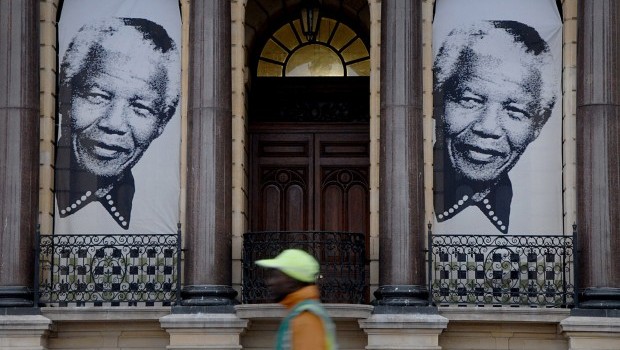 A pedestrian walks beneath two giant portraits outside the City Hall in Cape Town, South Africa, Monday, June 24, 2013 at the spot where, on the balcony, former South Africa president Nelson Mandela, made his first public speech after being released from 27 years imprisonment (AP Photo/Masixole Feni)