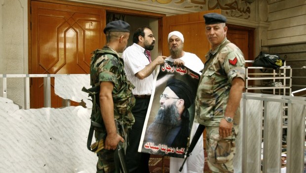 Supporters of radical Sunni cleric Sheikh Ahmad al-Assir carry a poster bearing his portrait next to members of the Lebanese Army at the entrance of the Bilal bin Rabah mosque in the Abra district of the southern city of Sidon on June 29, 2013. Source: AFP Photo/Mahmoud Zayyat