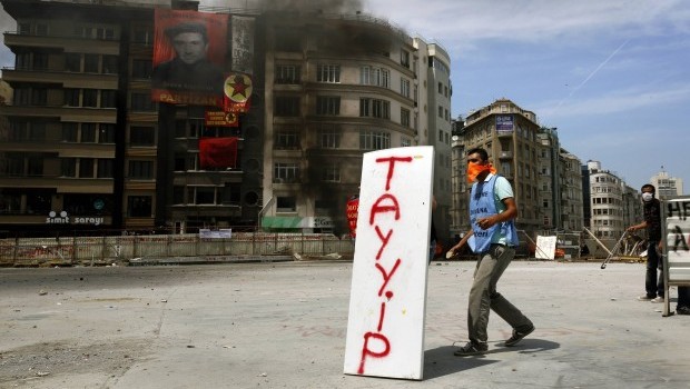 A protester takes cover behind a make-shift shield bearing the name of Turkish Prime Minister Tayyip Erdoğan during clashes between police and anti-government protesters, in Istanbul's Taksim Square June 11, 2013. Source: Reuters/Yannis Behrakis