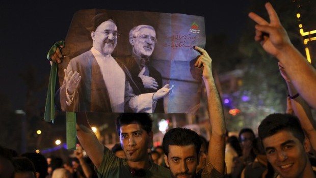 Iranians attend a street celebration, in Tehran, after their national soccer team qualified for the Brazil 2014 World Cup, after defeating South Korea, as they hold a poster of reformist former President Mohammad Khatami, left, and the Green Movement leader Mir Hossein Mousavi, who is currently under house arrest, on Tuesday, June 18, 2013 (AP Photo/Ebrahim Noroozi)