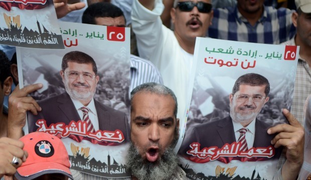 A supporter of the Muslim Brotherhood and Egypt's ousted president Mohamed Morsi (portrait) holds pictures of the former Islamist leader and shout slogans during a demonstration in the coastal city of Alexandria on July 19, 2013.  (AFP PHOTO / STR.)
