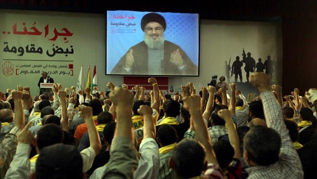 Hezbollah supporters raise their hands in salute as Hezbollah leader Sheik Hassan Nasrallah speaks on a screen via a video link from a secret place, during a rally to mark the "wounded resistant men day," in the southern suburb of Beirut, Lebanon, Friday, June 14, 2013. (AP Photo/Bilal Hussein)