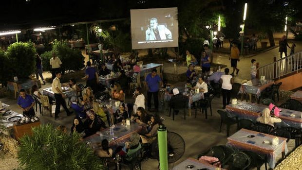 In this picture taken on Wednesday July 24, 2013, Lebanese and Syrian citizens gather at an outdoor coffee shop, as one of the Syrian popular series Al-Wiladah Men Al-Khasira (Birth from the Waist), is broadcast on a giant screen, in Beirut, Lebanon. (AP Photo/Hussein Malla)