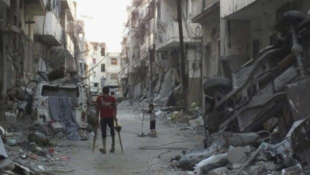 A man walks with makeshift crutches along a damaged street filled with debris in the besieged area of Homs August 6, 2013. (REUTERS/Yazan Homsy.)