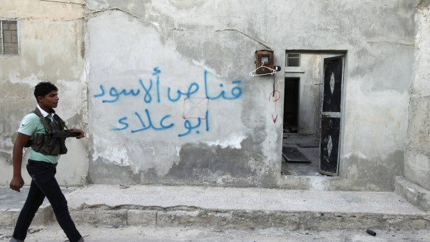 A Free Syrian Army fighter holding a weapon, walks past writing on the wall that reads, "Sniper of lions Abou Alaa" on a street near Nairab military airport, in Aleppo August 9, 2013. REUTERS/Nour Kelze (SYRIA - Tags: CONFLICT CIVIL UNREST)