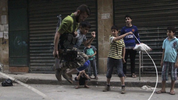 A member of the Free Syrian Army plays with children along a street in Aleppo's Bustan al-Qasr district August 23, 2013. Picture taken August 23, 2013. (REUTERS/Loubna Mrie)