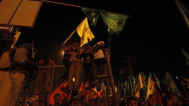 Palestinians celebrate and wave green Hamas and yellow Fatah flags as they wait for the released prisoners at a checkpoint at the entrance of Beit Hanoun between north of Gaza Strip and Israel, Tuesday, Aug. 13, 2013. (AP photo/Hatem Moussa)
