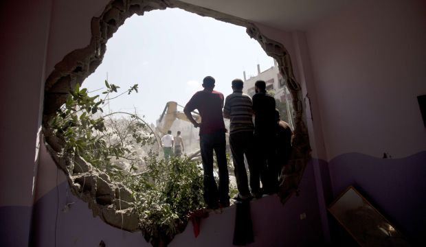 Palestinians stand watching from a whole in a wall as Civil Defense workers remove the rubble of a building destroyed in an Israeli air strike, in Gaza City, on July 21, 2014. (AFP PHOTO / MAHMUD HAMS)