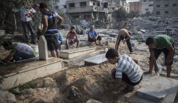 A Palestinian man looks on while others clean up graves from debris from a nearby house which was destroyed during an Israeli airstrike during the Muslim holiday of Eid Al-Fitr on the Sheikh Aduwan cemetery in Gaza City, on July 28 2014. (EPA/OLIVER WEIKEN)