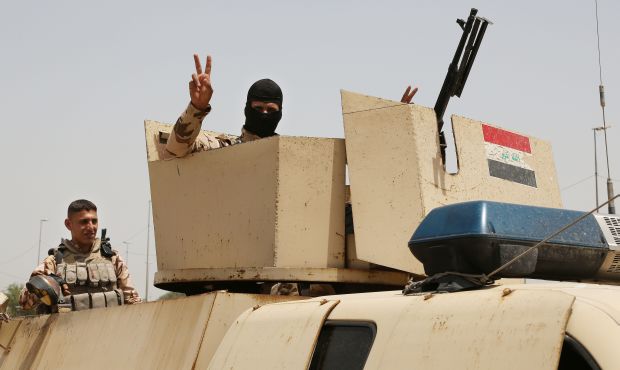 An Iraqi soldier flashes a V for victory sign while Iraqi men gather outside of the main army recruiting center to volunteer for military service in Baghdad, Iraq, on Thursday, June. 12, 2014. (AP Photo/ Karim Kadim)