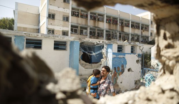 A Palestinian man pictured through a damaged classroom carries a boy as he walks past a UN-run school sheltering displaced Palestinians  in the northern Gaza Strip on July 30, 2014. (Reuters/Suhaib Salem)