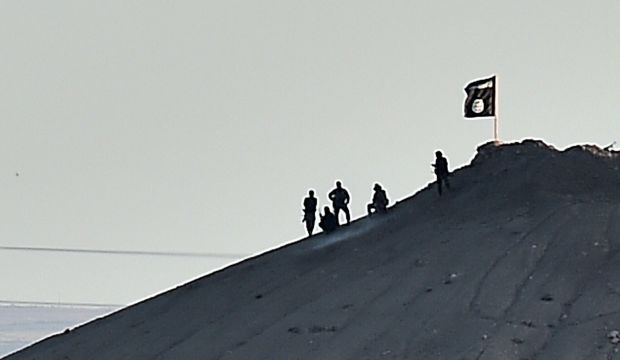 Alleged Islamic State of Iraq and Syria (ISIS) militants stand next to their flag atop a hill in the Syrian town of Ain Al-Arab, known as Kobani by the Kurds, as seen from the Turkish–Syrian border, on October 6, 2014. (AFP Photo/Aris Messinis)
