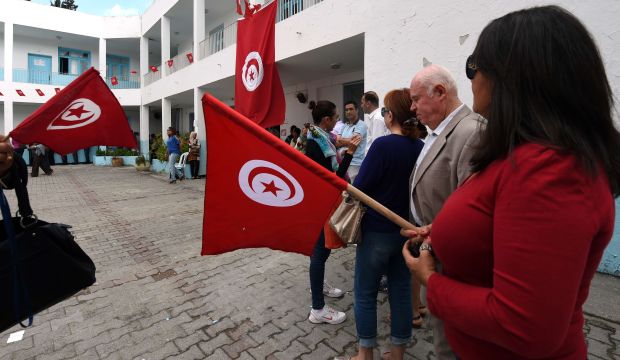 Tunisians wave their national flag as they queue outside a polling station at a school in Tunis to vote in the country's first post-revolution parliamentary election on October 26, 2014.(AFP PHOTO / FETHI BELAID)