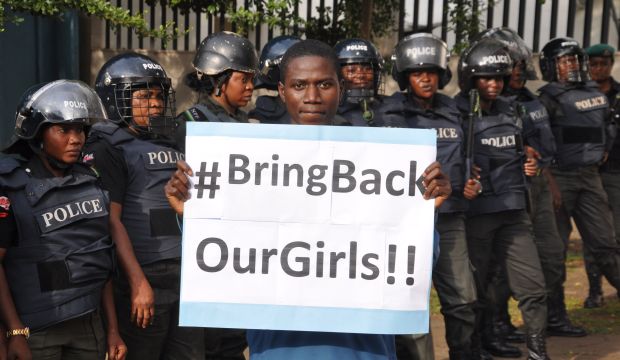 A man poses with a sign in front of police officers in riot gear during a demonstration calling on the government to rescue the kidnapped girls, in Abuja, Nigeria, on October 14, 2014. (AP Photo/Olamikan Gbemiga)