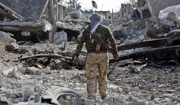 In this Wednesday, November 19, 2014 photo, a Kurdish People's Protection Units (YPG) fighter shows the extent of the damage from a truck bomb in Kobani, Syria. (AP Photo/Jake Simkin)