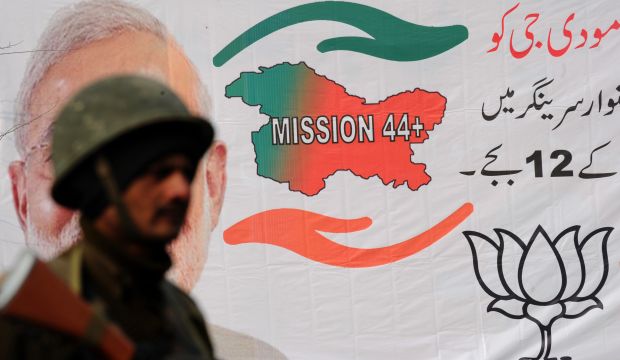 An Indian paramilitary soldier looks on as he obscures the image of Indian Prime Minister Narendra Modi on a Bharatiya Janata Party campaign poster , during a curfew in Srinagar on December 8, 2014. (AFP PHOTO/Rouf BHAT)
