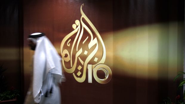 In this Wednesday, November 1, 2006 file photo, a Qatari employee of the Al-Jazeera Arabic-language TV news channel passes by the logo of Al-Jazeera in Doha, Qatar. (AP Photo/Kamran Jebreili, File)