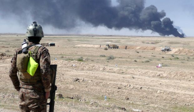 An Iraqi security forces member stands looking at smoke billowing from the Ajeel oil field located 35km (22 miles) northeast of Tikrit on March 11, 2015. (AFP/William G. Dunlop)