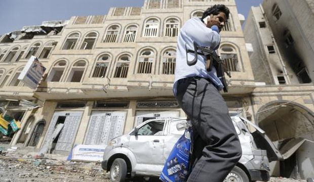 A man carrying a weapon talks on his mobile phone near a building damaged by an airstrike on a nearby Scud missile base in Yemen's capital Sana'a, on April 20, 2015. (Reuters)
